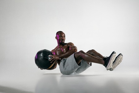 Preparing for the best. Young african-american bodybuilder training over grey background. Muscular single male model in sportwear with the ball. Concept of sport, bodybuilding, healthy lifestyle.の写真素材