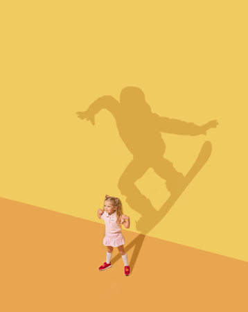 Its easy to fly. Childhood and dream concept. Conceptual image with child and shadow on the yellow studio wall. Little girl want to become snowboarding sportswoman, champion, winner.の写真素材