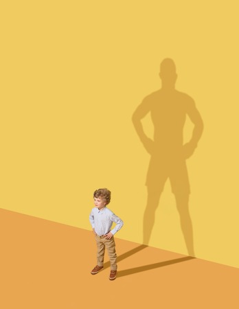 I could protect my family. Future champion. Childhood and dream concept. Conceptual image with child and shadow on the yellow studio wall. Little boy want to become a boxer and to build a sport career.の写真素材