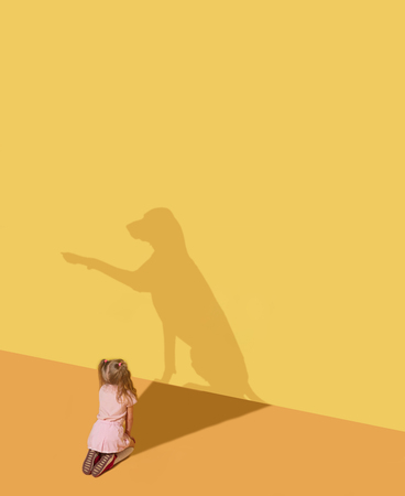 Pets make home more comfortable. Childhood and dream concept. Conceptual image with child and shadow on the yellow studio wall. Little girl want to have a dog and get a real faithful friend.の写真素材