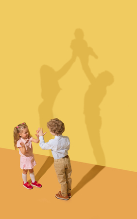 Happiness. Childhood and dream concept. Conceptual image with child and shadow on the yellow studio wall. Little boy and girl want to become parents and get big and friendly family together.の写真素材