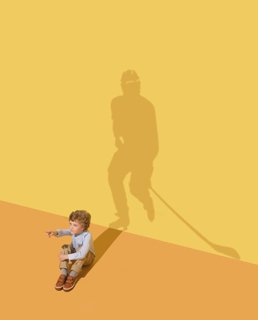 Ice and stands are calling. Childhood and dream concept. Conceptual image with child and shadow on the yellow studio wall. Little boy want to become hockey player and to build a sport career.の写真素材