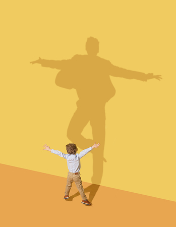 Succesfull. Childhood and dream concept. Conceptual image with child and shadow on the yellow studio...