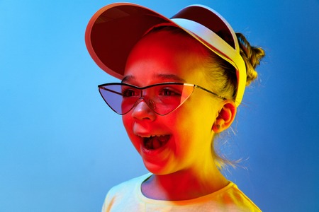 Happy teen girl standing and smiling isolated on trendy blue neon studio background. Beautiful...