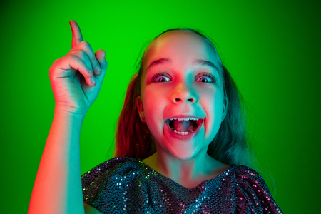 Wow. Beautiful female half-length portrait over green neon lights studio backgroud. Young emotional surprised teen girl standing with open mouth. Human emotions, facial expression concept. Trendy colorsの写真素材