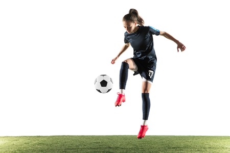 Young female football or soccer player with long hair in sportwear and boots kicking ball for the goal in jump isolated on white background. Concept of healthy lifestyle, professional sport, hobby.の写真素材