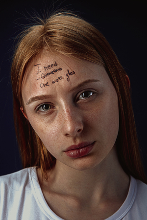 Portrait of young woman with mental health problems. Tattoo on the forehead with the words I need someone-one more glass. Concept of hidding the true feelings, psycological trouble, treatment.の写真素材