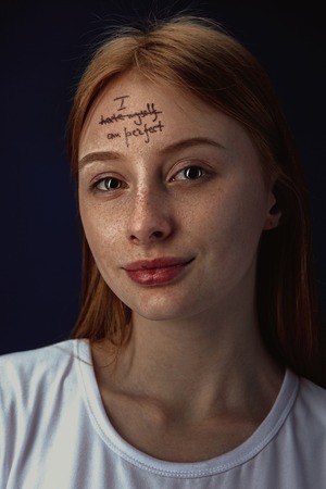 Portrait of young woman overcoming mental health problems. Tattoo on the forehead with the words I hate myself-perfect. Concept of psycological treatment, rehabilitation, return to healthy lifestyle.の写真素材