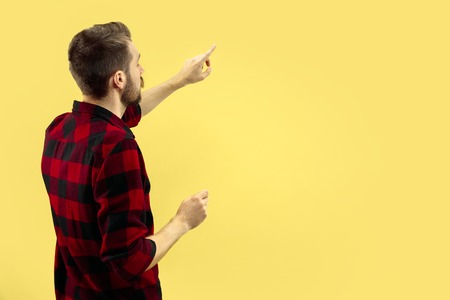 Half-length close up portrait of young man in shirt on yellow background. The human emotions, facial expression concept. Front view. Trendy colors. Negative space. Showing or pointing.の写真素材