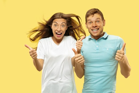 Beautiful young couples half-length portrait on yellow studio background. Woman and man in shirts...
