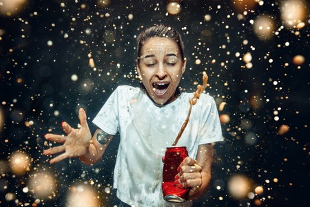 Woman drinking a cola at studio. Young smiling happy caucasian girl opening can with cola and...