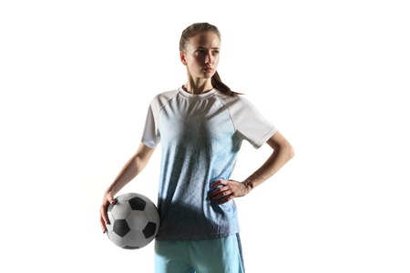 Young female football or soccer player with long hair in sportwear and boots standing with the ball isolated on white background. Concept of healthy lifestyle, professional sport, hobby.の写真素材