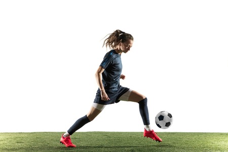 Young female football or soccer player with long hair in sportwear and boots kicking ball for the goal in jump isolated on white background. Concept of healthy lifestyle, professional sport, hobby.の写真素材