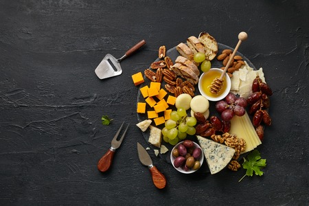 Top view of tasty cheese plate with fruit, grape, nuts and honey on a circle kitchen plate on the...