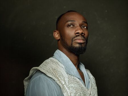 Young man as a medieval grandee or nobleman on dark studio background. Looking serious. Portrait of male model in retro costume. Human emotions, comparison of eras and facial expressions concept.の写真素材