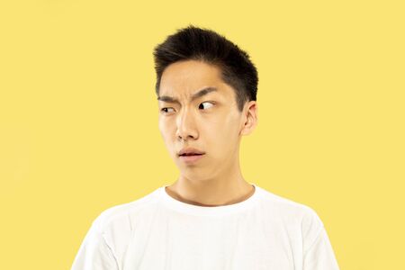 Korean young mans half-length portrait on yellow studio background. Male model in white shirt....