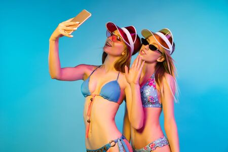 Beautiful young girls half-length portrait isolated on blue studio background in neon light. Women...