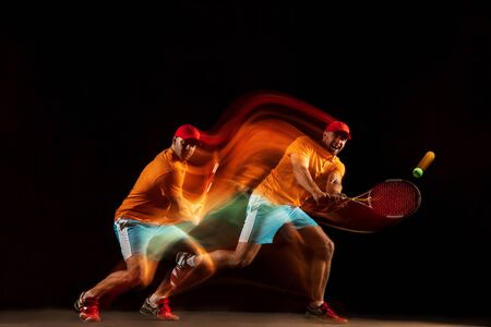 One caucasian man playing tennis isolated on black background in mixed light. Studio shot of fit...