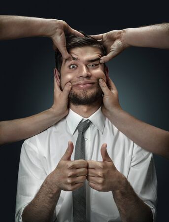 A male model surrounded by hands like his own thoughts on dark background. A young man pretending to be happy and showing the sign of ok. Concept of mental problems, troubles in work, indecision.の写真素材