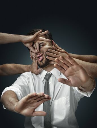 A male model surrounded by hands like his own thoughts on dark background. A young man doubts, cant...