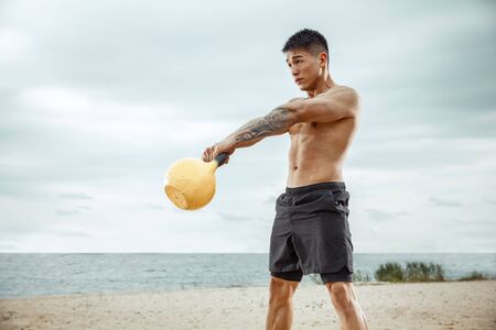 Young healthy man athlete doing exercise with the weight at the beach. Signle male model shirtless training at the river side in sunny day. Concept of healthy lifestyle, sport, fitness, bodybuilding.の写真素材