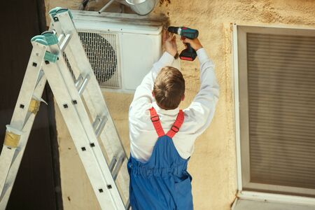 HVAC technician working on a capacitor part for condensing unit. Male worker or repairman in uniform...