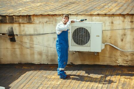 HVAC technician working on a capacitor part for condensing unit. Male worker or repairman in uniform repairing and adjusting conditioning system, diagnosting and looking for technical issues.の写真素材