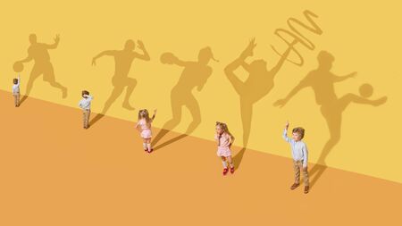 Childhood and dream concept. Conceptual image with children and shadow on the yellow studio wall. Little girl and boy want to become gymnast, dancer, artist, boxer, runner or football player.の写真素材