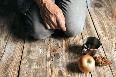 Male beggar hands seeking food or money with coins tin from human kindness on the wooden floor at public path way, street walkway. Homeless poor in the city. Problems with finance, place of residence.の写真素材