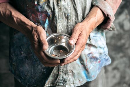 Male beggar hands seeking food or money with coins tin from human kindness on the wooden floor at public path way, street walkway. Homeless poor in the city. Problems with finance, place of residence.の写真素材