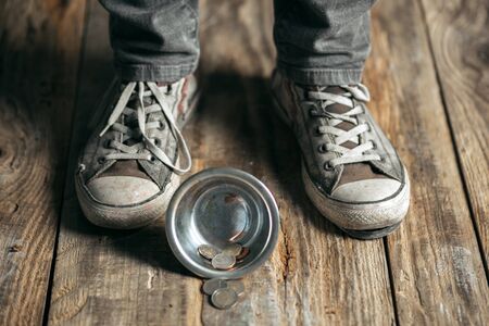 Male beggar hands seeking food or money with coins tin from human kindness on the wooden floor at public path way, street walkway. Homeless poor in the city. Problems with finance, place of residence.の写真素材