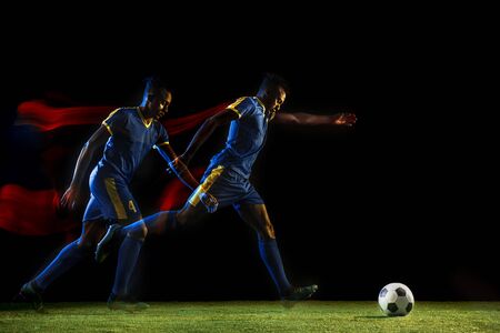 Young african-american male football or soccer player in sportwear and boots kicking ball for the goal in mixed light on dark background. Concept of healthy lifestyle, professional sport, hobby.の写真素材
