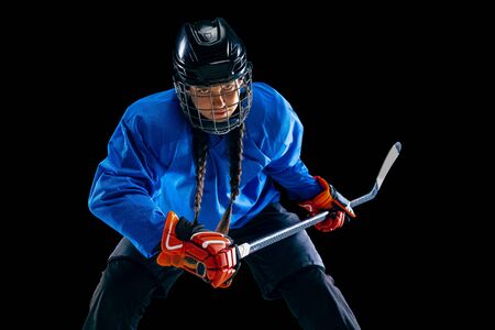 Young female hockey player with the stick isolated on black background. Sportswoman in action wearing equipment attacking for the goal or score. Concept of sport, healthy lifestyle, motion, movement.の写真素材