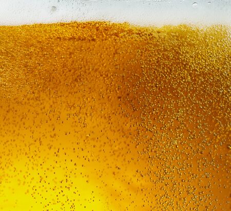 Close up view of floating bubbles in light golden colored beer