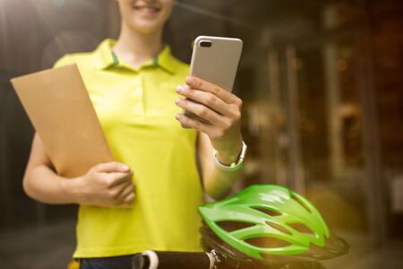 Young woman in yellow shirt delivering package using gadgets to track order at the citys street. Courier using online app for receiving payment and tracking shipping address. Modern technologies.の写真素材