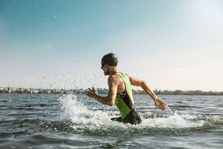 Professional triathlete swimming in rivers open water. Man wearing swim equipment practicing triathlon on the beach in summers day. Concept of healthy lifestyle, sport, action, motion and movement.の写真素材