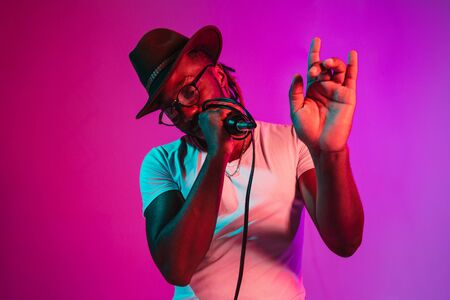 Young african-american jazz musician with microphone singing a song on purple studio background in...