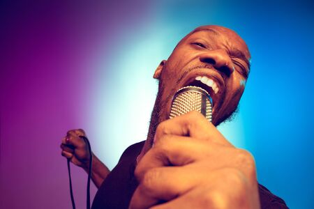 Young african-american jazz musician singing a song on gradient purple-blue background. Concept of...