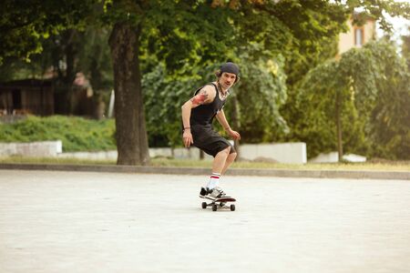 Skateboarder doing a trick at the citys street in cloudly day. Young man in sneakers and cap riding and longboarding on the asphalt. Concept of leisure activity, sport, extreme, hobby and motion.の写真素材
