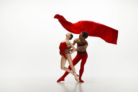 Graceful classic ballet dancers dancing isolated on white studio background. Couple in bright red clothes like a combination of wine and milk. The grace, artist, movement, action and motion concept.の写真素材