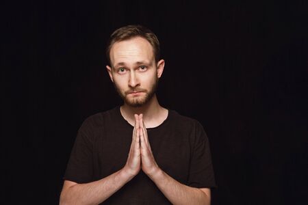 Close up portrait of young man isolated on black studio background. Photoshot of real emotions of...