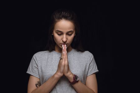 Close up portrait of young woman isolated on black studio background. Photoshot of real emotions of female model. Praying with closed eyes, sad and hopeful. Facial expression, human emotions concept.の写真素材