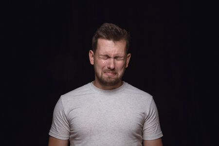 Close up portrait of young man isolated on black studio background. Photoshot of real emotions of male model. Crying with closed eyes, sad and hopeless. Facial expression, human emotions concept.の写真素材