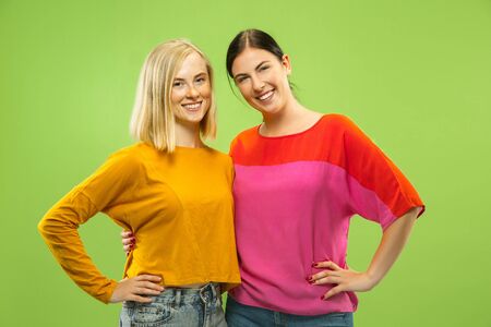 Portrait of pretty charming girls in casual outfits isolated on green studio background. Two female models as a girlfriends or lesbians. Concept of LGBT, equality, human emotions, love, relation.の写真素材