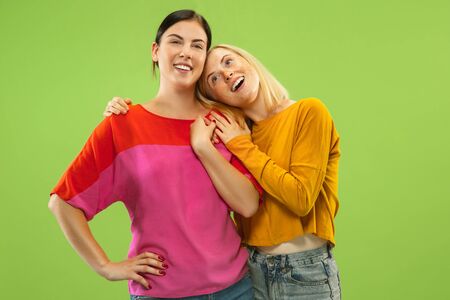 Portrait of pretty charming girls in casual outfits isolated on green studio background. Two female models as a girlfriends or lesbians. Concept of LGBT, equality, human emotions, love, relation.の写真素材
