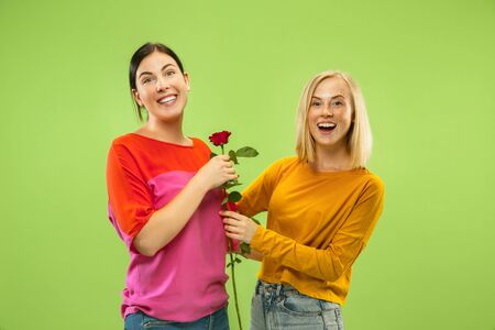 Portrait of pretty charming girls in casual outfits isolated on green studio background. Two female models as a girlfriends or lesbians. Concept of LGBT, equality, human emotions, love, relation.の写真素材