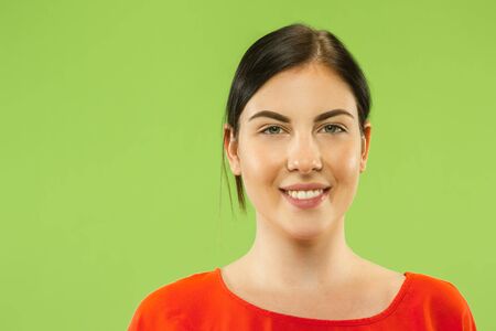 Caucasian young womans close up portrait on green studio background. Brunette female model in red shirt smiling and looks happy. Concept of human emotions, facial expression.の写真素材