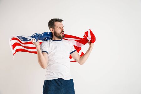 Celebrating an Independence day. Stars and Stripes. Young man with the flag of the United States of America isolated on white studio background. Looks crazy happy and proud as a patriot of his country.の写真素材