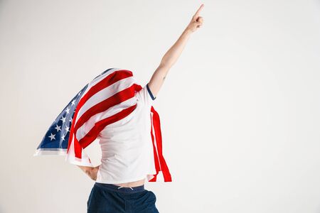 Celebrating an Independence day. Stars and Stripes. Young man with the flag of the United States of America isolated on white studio background. Looks crazy happy and proud as a patriot of his country.の写真素材
