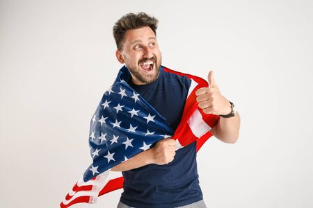 Celebrating an Independence day. Stars and Stripes. Young man with the flag of the United States of America isolated on white studio background. Looks crazy happy and proud as a patriot of his country.の写真素材